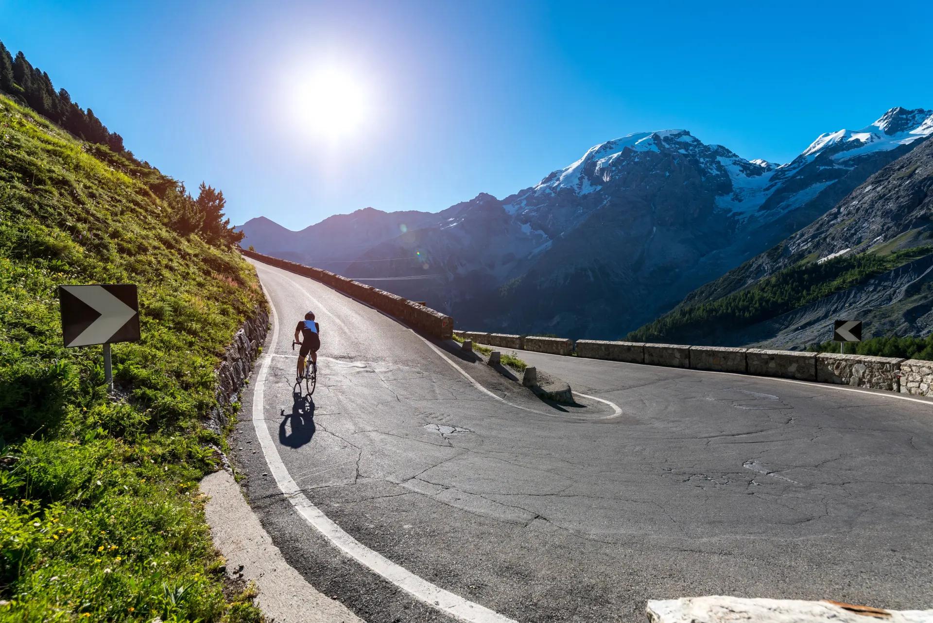 Cyclist climbing a sunlit alpine mountain pass